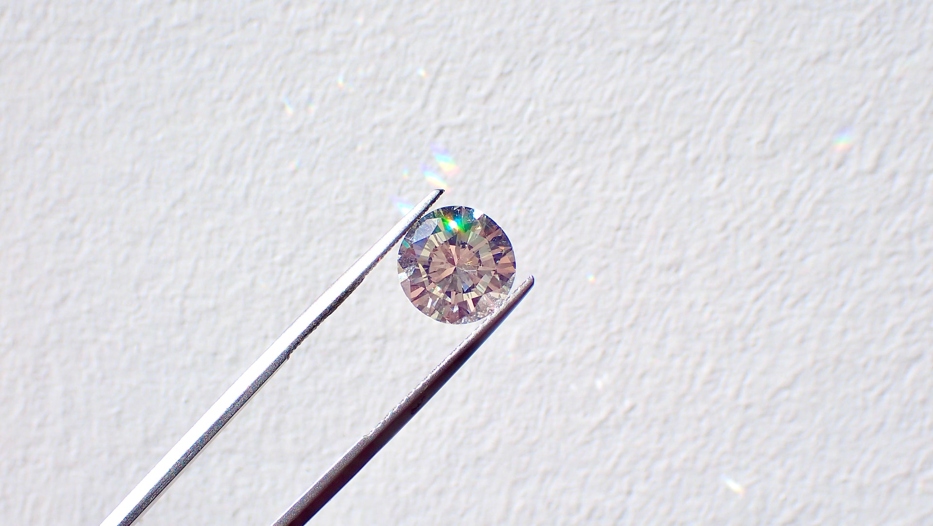 close up image of a round cut diamond held between a pair of tweezers against a white background