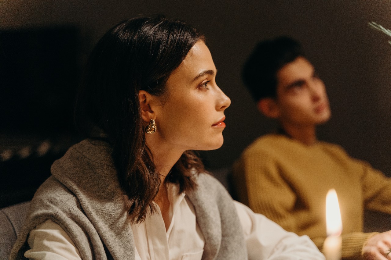 lady wearing a gold earring with a candle and a man in the background