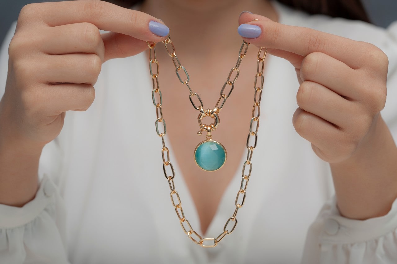 a lady holding a gold chain and blue gemstone pendant