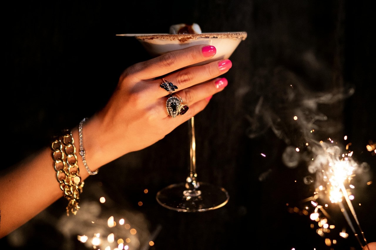 A woman toasting the New Year with sapphire and diamond statement rings, gold bracelets, and a diamond tennis bracelet