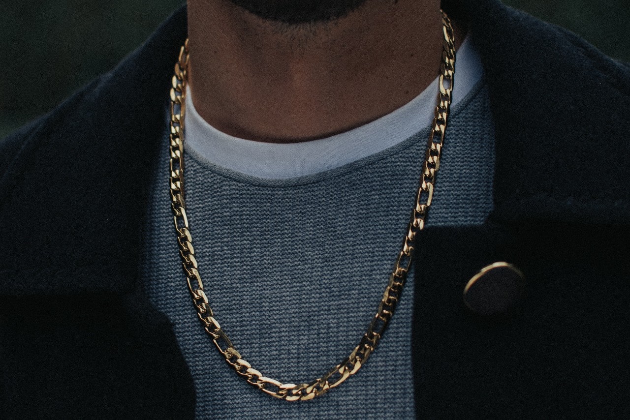 A close-up image of a man’s neckline adorned with a yellow gold chain necklace.