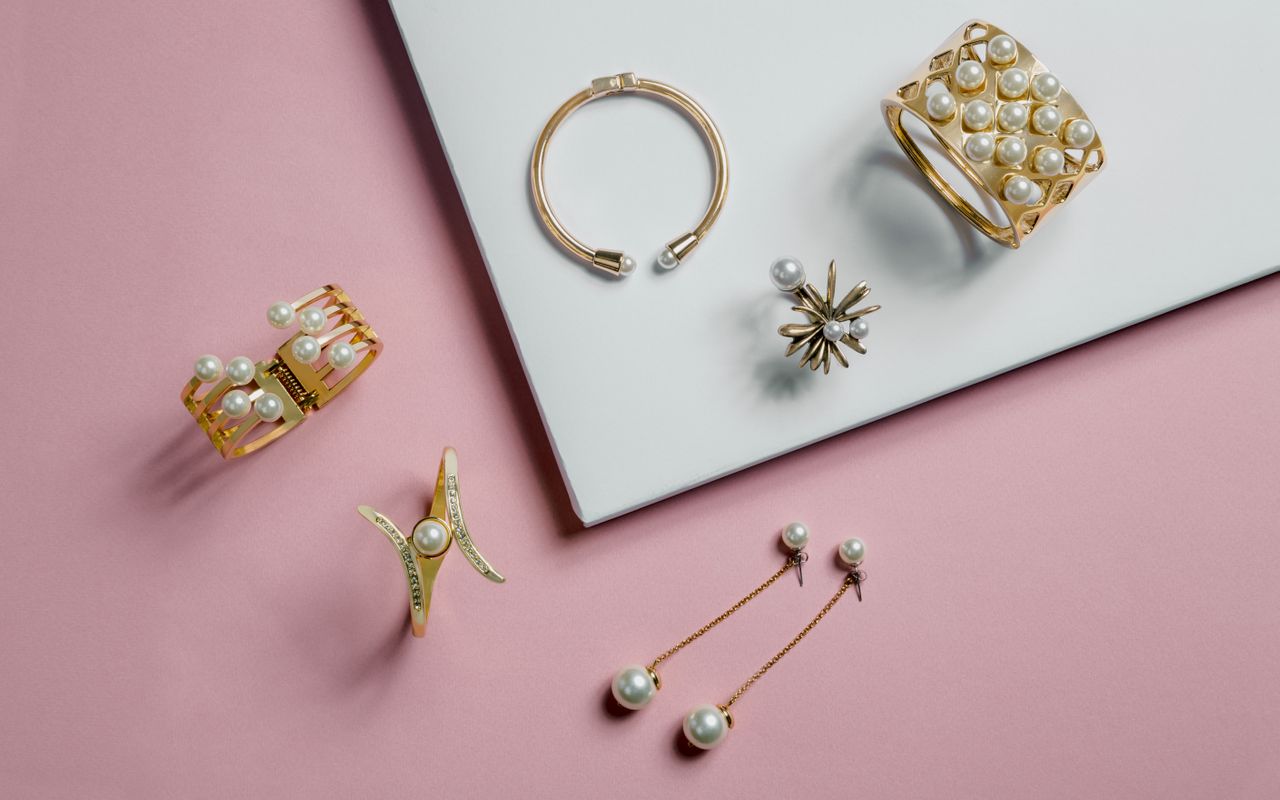 A set of gold and pearl jewelry against a pink and white background
