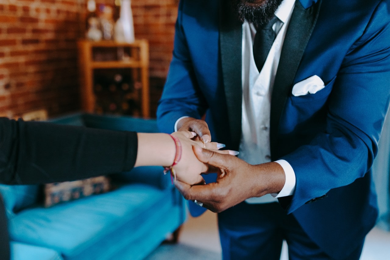 A woman’s outstretched hand being fitted with an engagement ring by a person in a suit